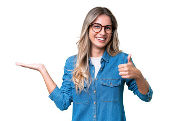 Young Uruguayan woman over isolated background holding copyspace imaginary on the palm to insert an ad and with thumbs up - obrazy, fototapety, plakaty