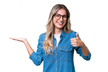 Young Uruguayan woman over isolated background holding copyspace imaginary on the palm to insert an ad and with thumbs up