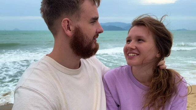 young happy couple in love on a honeymoon in bad weather, on vacation make a video selfie , sea background, the concept of a sweet relationship, kiss