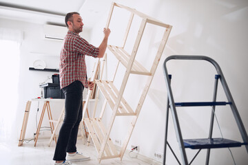 Man assembling new wooden shelf and furniture in the apartment.
