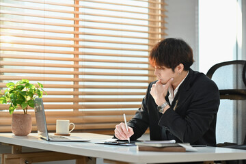 Professional businessman in smart suit looking at laptop screen, working statistical data at his office