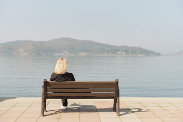 Beautiful adult woman sits after a walk on a bench and looks at the sea and blue sky, space for text idea for background