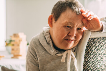 Portrait of an elderly smiling woman with Down syndrome in a sunny room