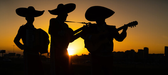 Silhouettes of a mexican musicians mariachi band on a background of city panorama. 