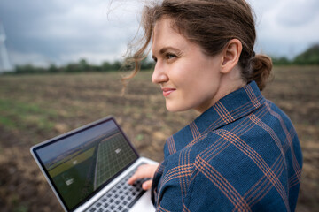 Farmer with laptop on the field. Wind turbines on a horizon. Smart sustainable farming and...