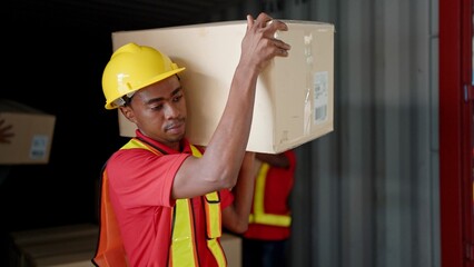 Young African American black workers courier lifting cargo boxes stacking on pallet in warehouse wearing engineer suit and helmet for safety. Shipment boxes. Warehousing storage