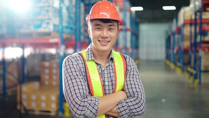 Asian worker standing in large warehouse distribution center with arms crossed in shelves with...