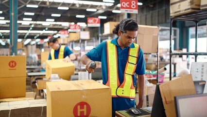 Warehouse worker using a QR code reader, scanning parcels into the system while working inside a...