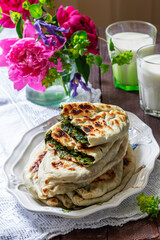 Traditional Armenian flatbread with greens zhengyalov hats, served with yogurt on the background of a bouquet.