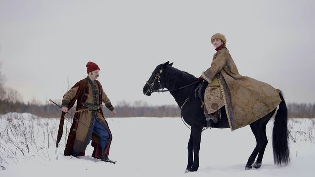 A male warrior trains his horse in a field of tricks. Vintage style of clothing riding horses in the countryside on a winter day