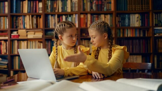 Funny twin sisters arguing while doing homework in library, sibling rivalry
