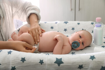 Mother changing baby's diaper on table indoors, closeup