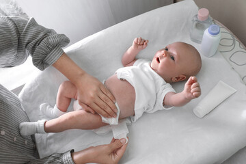 Mother changing her baby's diaper on table indoors, closeup