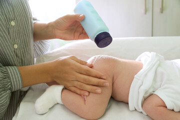 Mother applying dusting powder at baby's buttocks on changing table indoors, closeup