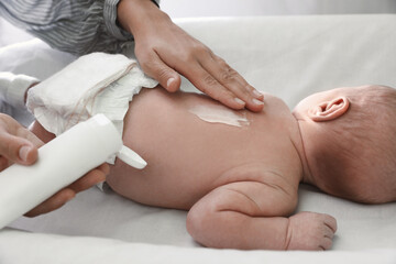 Mother applying moisturizing cream onto baby`s back on changing table, closeup