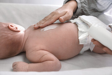 Mother applying moisturizing cream onto baby`s back on changing table, closeup