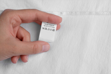 Woman holding clothing label on white garment, top view. Space for text