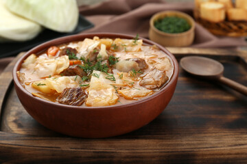 Tasty cabbage soup with meat, carrot and dill on wooden table, closeup