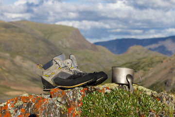 hiking boots, titanium mug and spoon on the background of the Alpine valleys. Objects in focus, background blurred.
