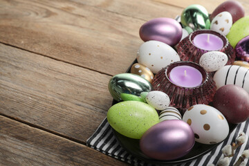Many beautifully decorated Easter eggs and scented candles on wooden table, space for text