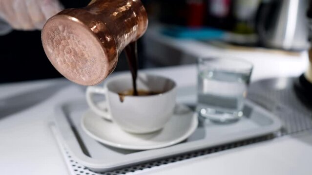barista pouring fresh hot coffee in cup from traditional turkish copper cezve, closeup view