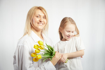 Blonde mother and daughter with bouquet of tulips on a white background. Mom and girl together on a holiday mother's day with flowers. Congratulations to women on International Women's Day on March 8