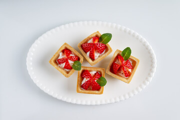 homemade tartlets with strawberries on a white plate, top view