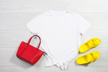 White female t shirt mock up flat lay on wooden background. Summer accessories. Yellow Flip flops, red bag. Top front view t-shirt copy space. Mockup tshirt summertime. Template blank shirt. - obrazy, fototapety, plakaty