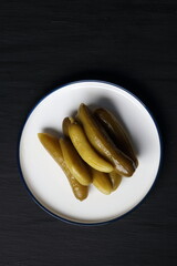 Cucumber pickles in a plate on a black background