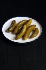 Cucumber pickles in a plate on a black background