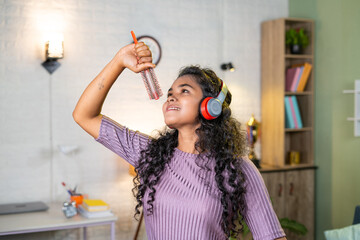Cheerful girl with wireless headset dancing by singing with hair comb at home - concept of entertainment, freedom and happiness
