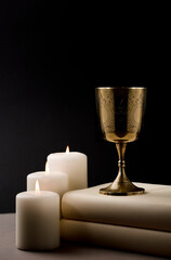golden christian chalice with burning candles on beige altar black background night