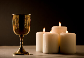 golden christian chalice with burning candles on beige altar black background night