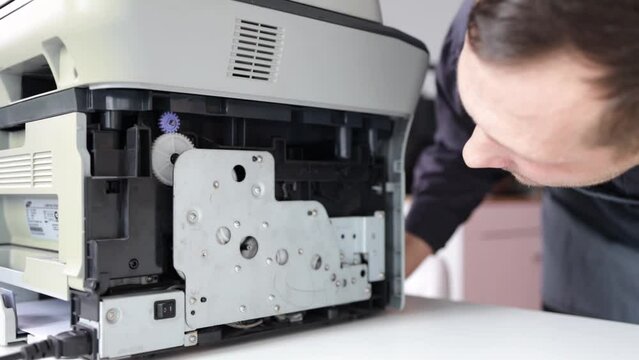printer repair technician. A male handyman inspects a printer before starting repairs in a client's apartment.