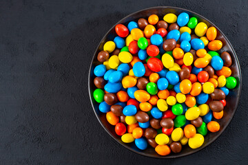 Multi-colored round candies in colored glaze in large quantities in a plate