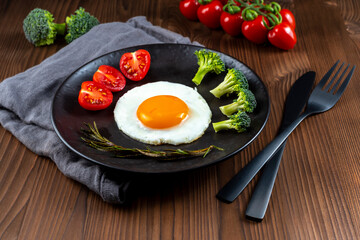 Fried soft-boiled egg on a black plate with fresh  vegetables 