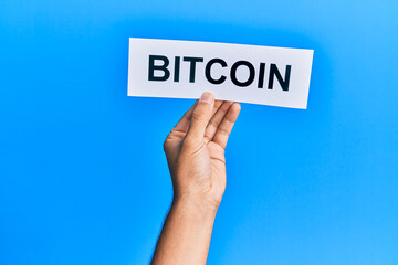 Hand of caucasian man holding paper with bitcoin word over isolated blue background