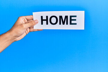 Hand of caucasian man holding paper with home word over isolated blue background