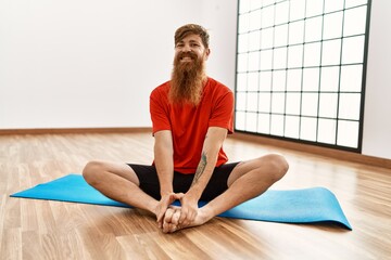 Young redhead man smiling confident stretching at sport center