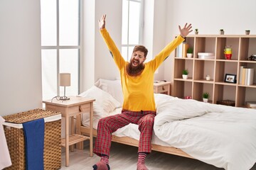 Fototapeta na wymiar Young redhead man waking up stretching arms yawning at bedroom