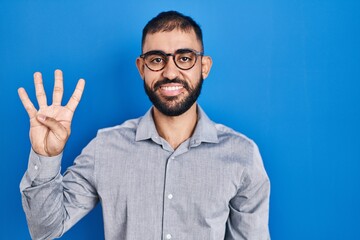 Fototapeta premium Middle east man with beard standing over blue background showing and pointing up with fingers number four while smiling confident and happy.