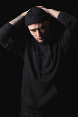 Studio portrait of handsome hipster guy wearing black blank hoodie or sweatshirt and hat. Mockup for print.