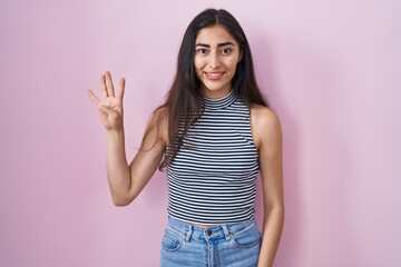 Young teenager girl wearing casual striped t shirt showing and pointing up with fingers number four while smiling confident and happy.