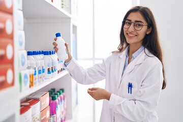 Young hispanic girl pharmacist organizing shelving at pharmacy