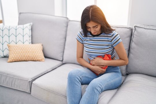 Young hispanic girl suffering for menstrual pain using hot water bag at home