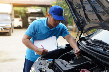 Fototapeta na wymiar Asian man mechanic wears blue cap and blue shirt, holds paper notepad, checking and analyzing car engine under the hood, found insect that causes engine broken .Concept, Outdoor car inspection service