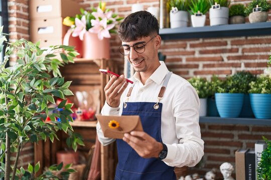 Young hispanic man florist talking on smartphone reading envelope letter at florist