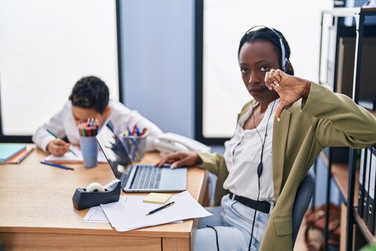Young mother wearing call center agent headset with angry face, negative sign showing dislike with thumbs down, rejection concept