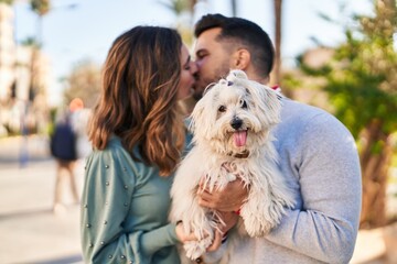 Man and woman holding dog standing together kissing at park