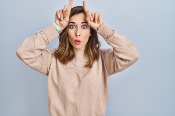 Fototapeta premium Young woman standing over isolated background doing funny gesture with finger over head as bull horns